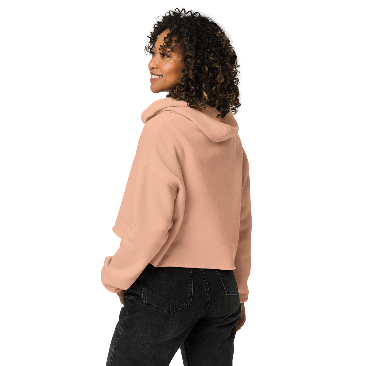 Woman wearing a dusty pink crop hoodie with a hood, showcasing the flattering cropped cut and soft fabric paired with black jeans.